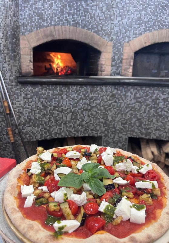 Pizza con pomodorini e mozzarella davanti al forno a legna acceso