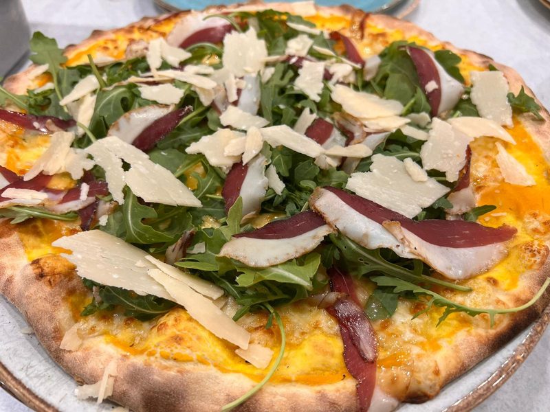 Pizza con rucola, affettato e scaglie di grana